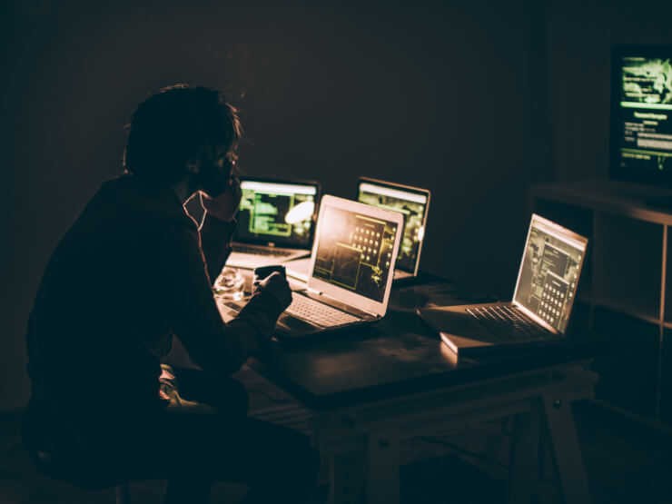 Figure sitting in front of several laptops